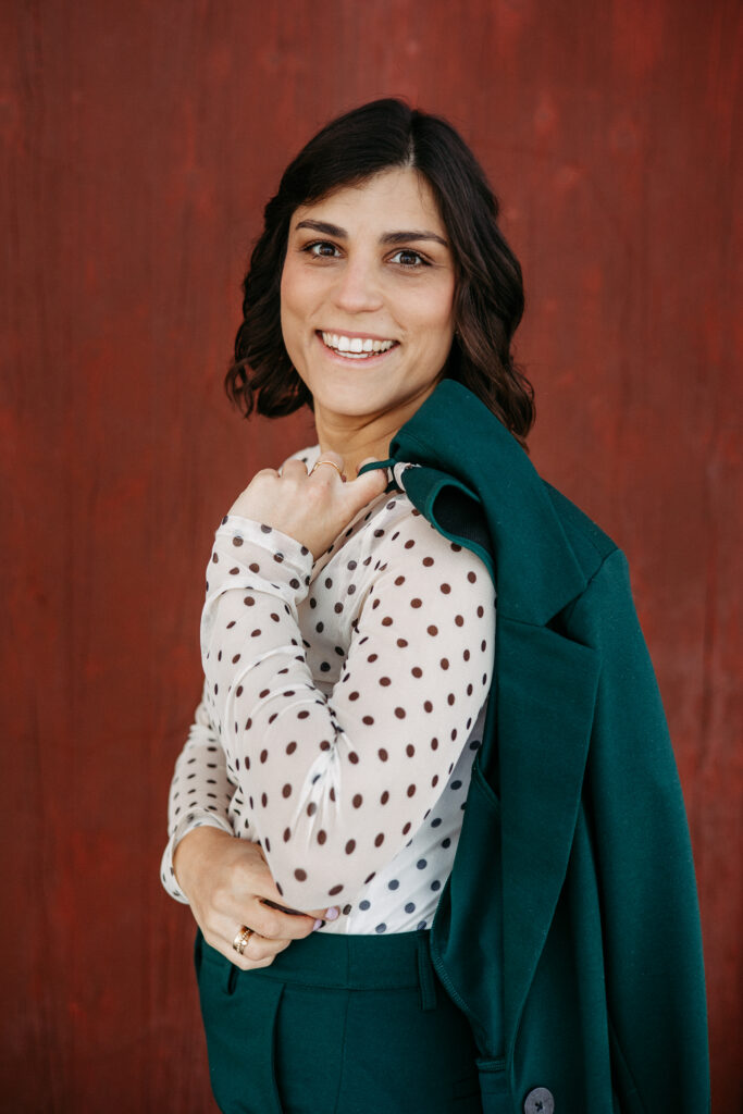 Bewerbungsbild, leicht von der Seite stehend, lächelnde Person. Jacket lässig über die Schulter geworfen, vor farbigem Hintergrund. Lockeres Businessfoto